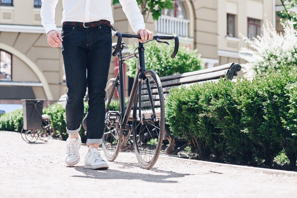 Close up outdoor image of young hipster man in jeans and shoes at stylish modern fix bike. Sunny